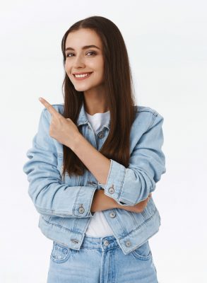 Smart good-looking, creative young brunette girl giving advice, pointing upper left corner, suggest promo, smiling pleased, approve some product, standing white background. Copy space